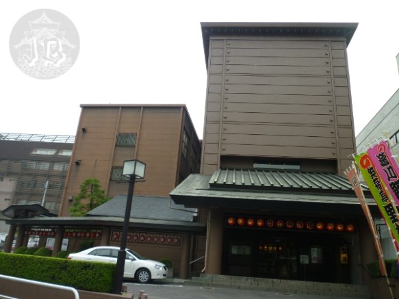 A shoebox-like building, in brown, with some reddish paper lanterns at the entrance