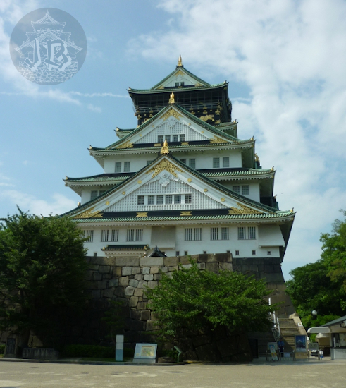 Osaka Castle. It stands on a rock base, and it has four floors. The roofs are green/grey and the main walls are white with golden decoration
