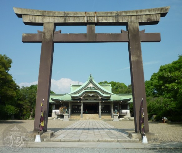 A severe grey torii in front of a white and green shrine building