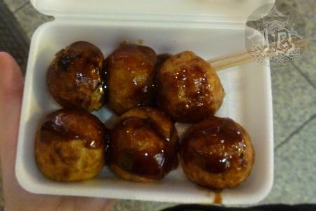 A box of six round dumplins covered with brown sauce