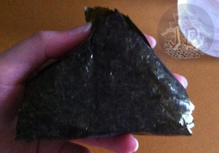 A close up of the onigiri. The triangle is made out of dry algae (nori), you can see the rice filling on one corner