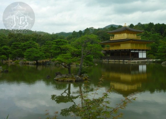 A pond with a pine tree at the centre. To the side, a three-story pavillion that looks similar to a pagoda. The first floor is built in wood and plaster, the upper ones have been covered in gold