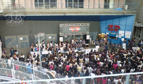 Entrance to the venue from above. Lots of people are waiting, a lot of them with pink shirts