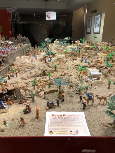 A Nativity made out of Playobil figurines, the stable is on the left and a bunch of toys are coming towards it through the desert. There a lots of dromedaries.
