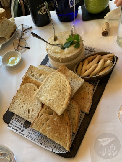A tray with bread slices and breadsticks, and a cream cheese with spoons to be spread on the bread