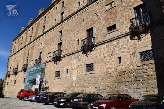 Plain building with ornate balconies, and cars parked on a row in front of it.
