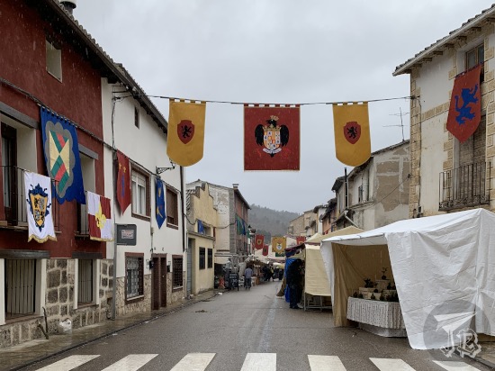 A wide street. There are flags hanging above and from the balconies, and shopping stands on the right. the sky is dark and heavy, as in all the pictures taken