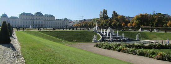 A huge garden with a palace in the background. The garden is artificial in a way, with perfectly-trimmed grass, fountains, and bushes.