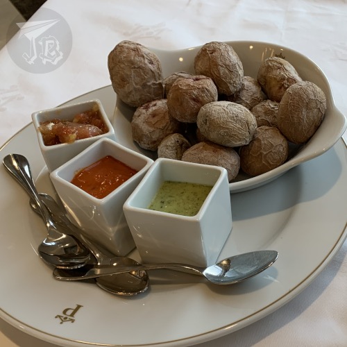 Small voiled potatoes and three small bowls of sauces. The potatoes are unpeeled and they look wrinkled.
