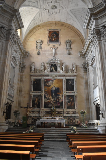 A Catholic altar showing the Inmaculate conception in the centre, she is dressed in blue, and standing in front of golden clouds, with angels around her. The back of the altar is built in white stone, and ornate.