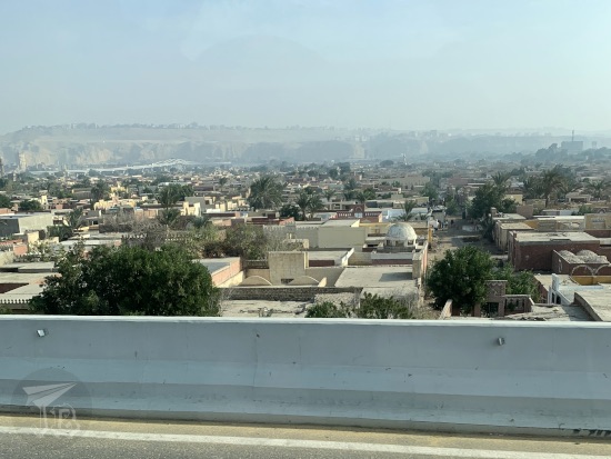 Cairo, City of the Dead from the moving bus. A bunch of low constructions with flat celings or domes, with some trees sprinkled inbetween.