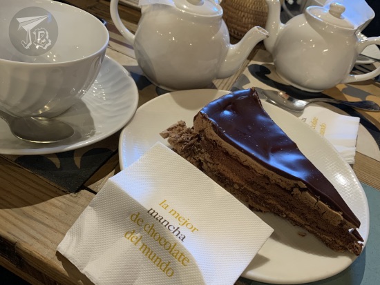 A slice of chocolate cake in front of mugs and teapots