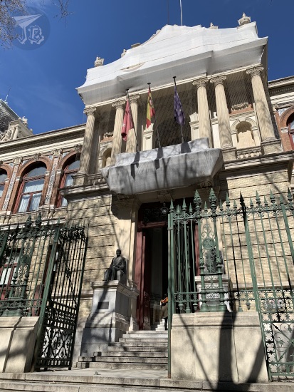 The ETSIME in Madrid. Pink-and-white building from the 19th century, accessible through stairs, with flags hanging over the door