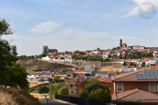 A general view of the town of Almadén. It shows that it is located on a hilltop. The main structures seen are the mining complex on the left (a grey mass on top of a black gorge) and the castle at the very top.