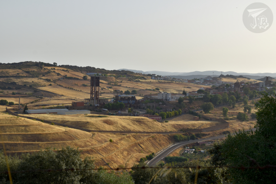 A general view of the town of Almadén. It shows that it is located on a hilltop. The main structures seen are the mining complex on the left (a grey mass on top of a black gorge) and the castle at the very top.