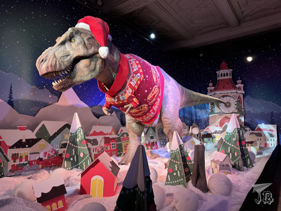 T Rex animatronic dressed in an ugly Christmas sweater with T Rex skulls.