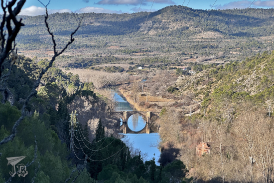 View from above of the valley, with the river crossed by an old bridge. The arch of the bridge and its reflection create a perfect circle